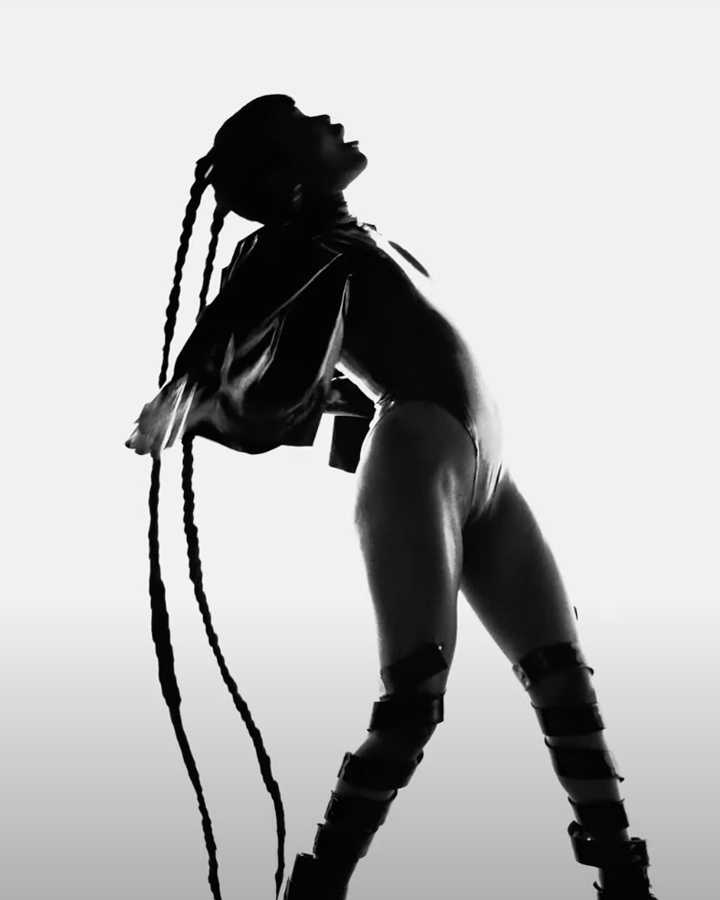 Black and white still of Tkay Maidza bending backwards with long braids against a white backdrop